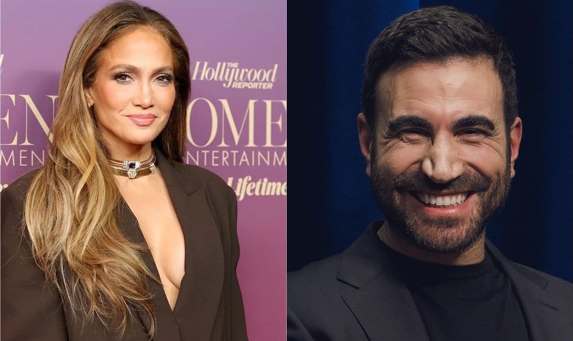 Jennifer Lopez smiling on a red carpet wearing an elegant outfit, with microphones and photographers visible in the background