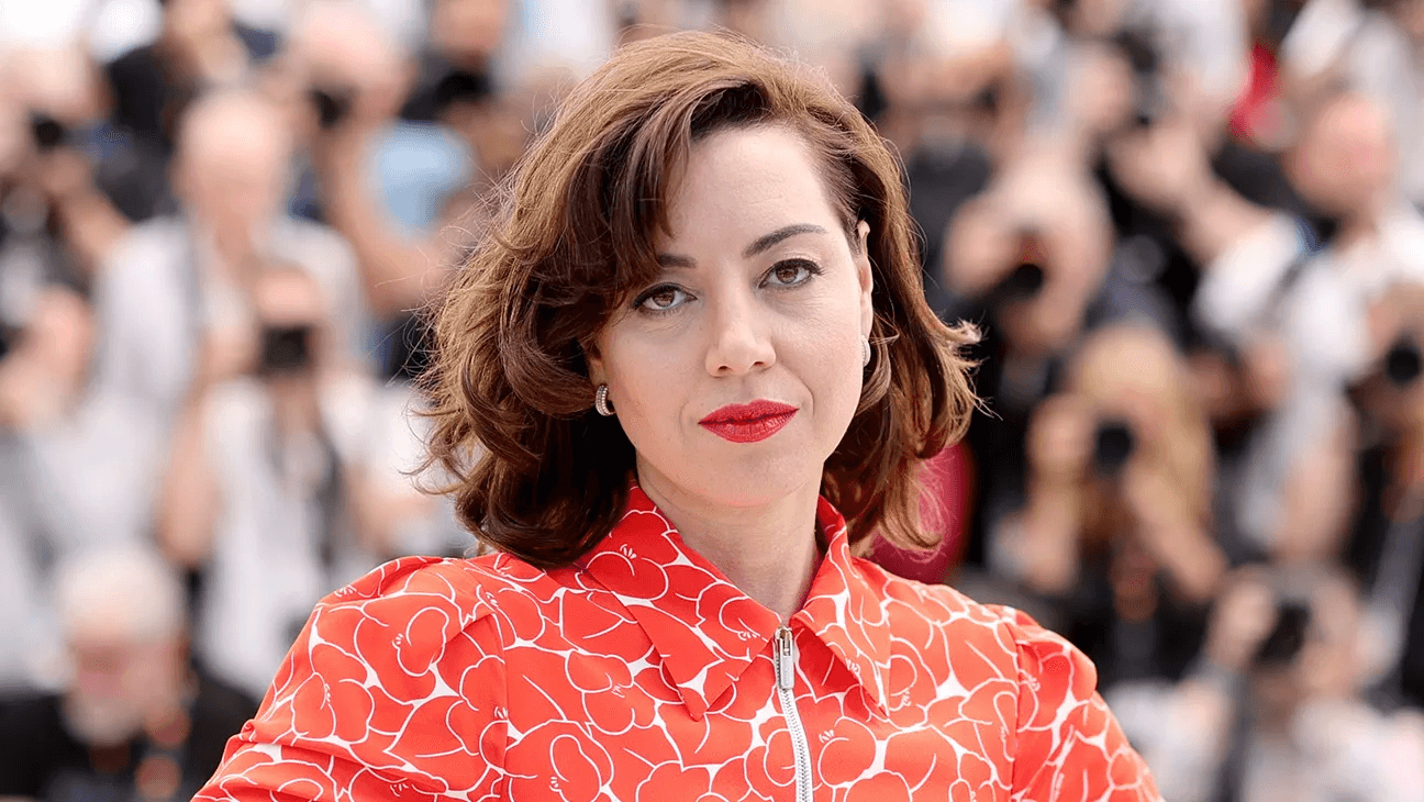 Aubrey Plaza cradling her baby bump in a white outfit on the red carpet at the Tribeca Festival premiere of The Accompanist in New York City