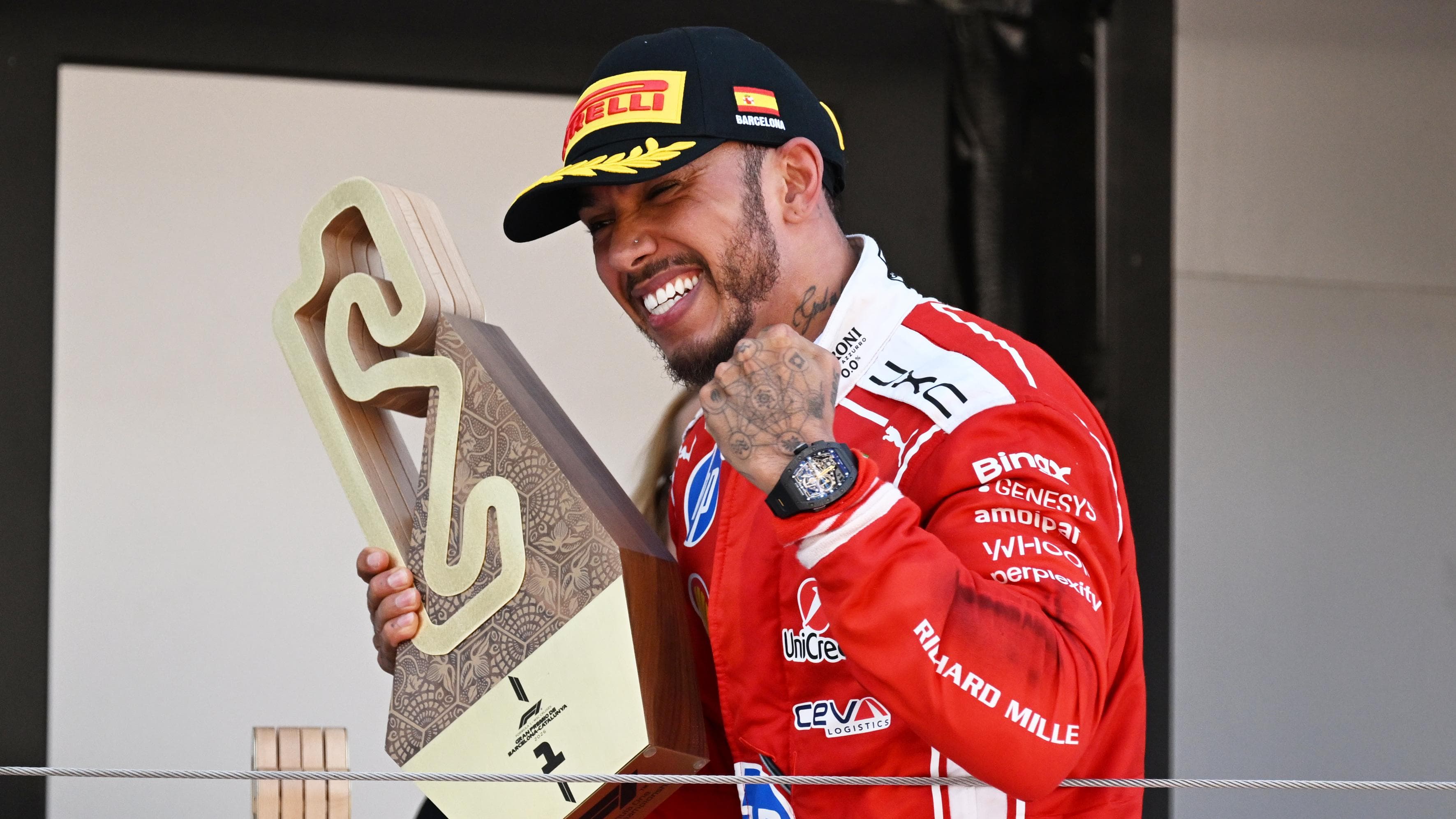 Lewis Hamilton celebrating in parc fermé at the Barcelona-Catalunya Circuit, wearing his red Ferrari race suit and holding a trophy after winning the Spanish Grand Prix