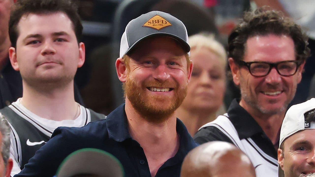 Prince Harry wearing a dark polo shirt and cap sitting courtside at the NBA Finals at Frost Bank Center in San Antonio, Texas