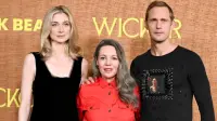 A woman in an elegant outfit and a tall man in formal attire stand together on the red carpet at the Wicker Los Angeles premiere, smiling for photographers