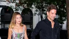 A man and a woman walking together on a city street, the woman wearing a casual outfit and the man in a relaxed ensemble, against an urban Parisian backdrop.