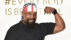 A man in a stars and stripes bandana and a graphic T-shirt, seen from the shoulders up during a video call, looking directly at the camera with a composed expression