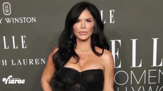 A woman in a black off-the-shoulder gown with a plunging neckline and a large diamond necklace walks alongside a man in a black tuxedo at a formal evening event