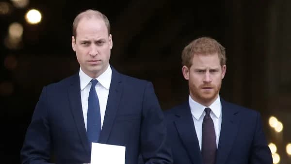 Two men in formal attire standing apart from one another at a public event, neither making eye contact