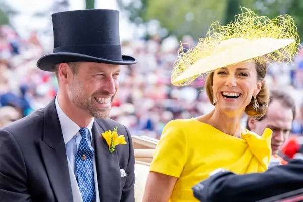 A man and woman dressed in smart casual clothing stand together at an outdoor public event, smiling and engaged with the crowd around them