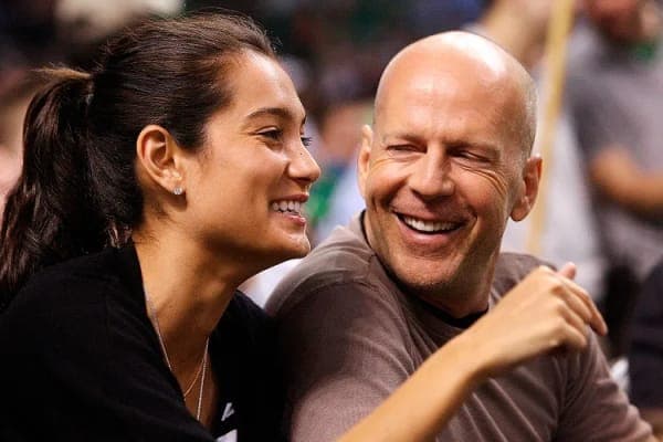 Emma Heming Willis wearing a birthday party hat alongside Bruce Willis, both smiling during a birthday celebration at home