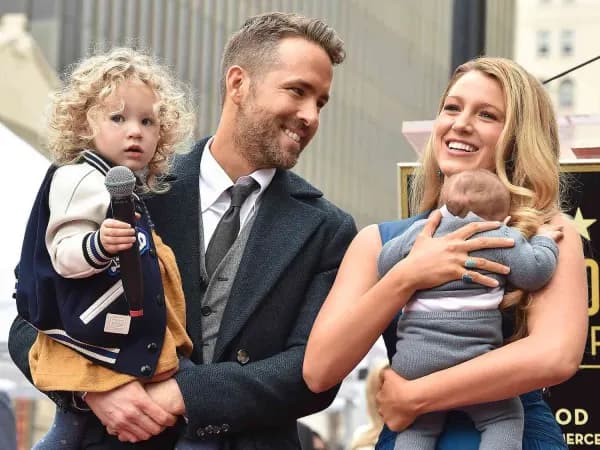 A man in casual clothing poses with a woman in a summery outfit, both smiling warmly, surrounded by young children whose faces are not visible in the image