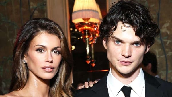 A young woman and a young man wearing Dior clothing standing close together against a neutral studio backdrop