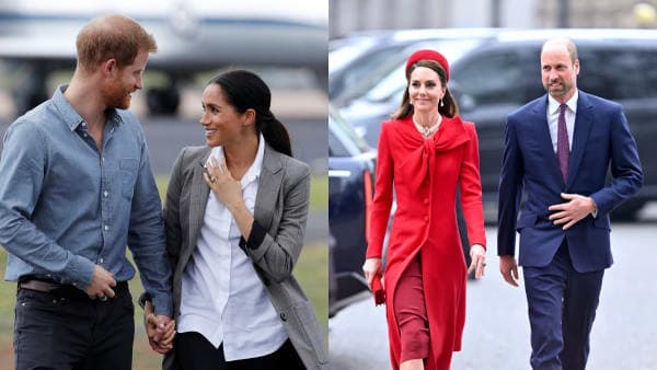 A man in a dark suit and a woman in a light-coloured coat walk together at a formal outdoor event, both smiling at a crowd