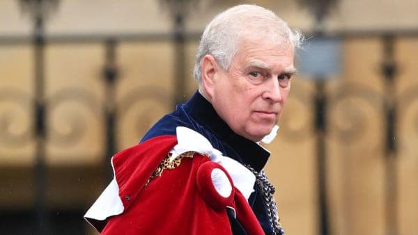 A middle-aged man in a dark suit walks out of a grand stone building, looking straight ahead with a neutral expression