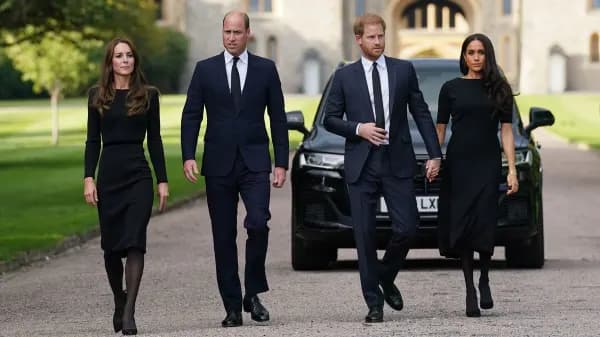 A woman in formal attire standing beside a man in a suit, both smiling and greeting members of the public at an outdoor royal engagement