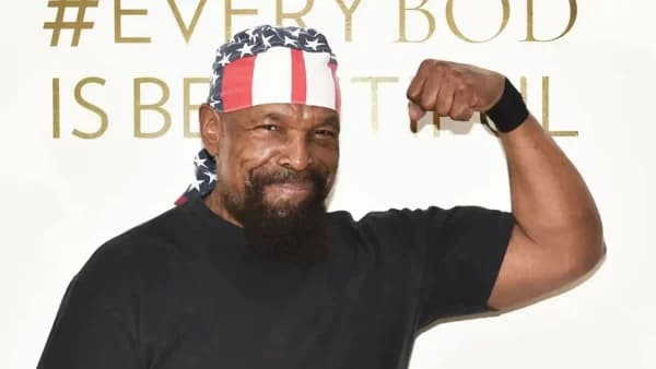 A man in a stars and stripes bandana and a graphic T-shirt, seen from the shoulders up during a video call, looking directly at the camera with a composed expression