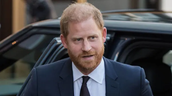 A man in a dark suit and tie smiling as he arrives at a formal evening event, pausing outside a hotel entrance to greet officials and pose for photographs