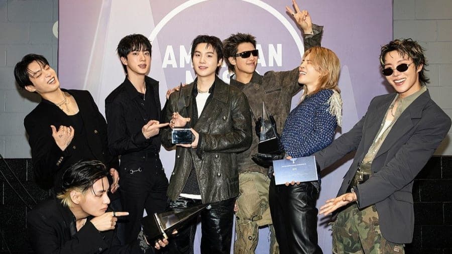 BTS members posing together at a public event, all seven dressed in coordinated outfits and smiling for the camera