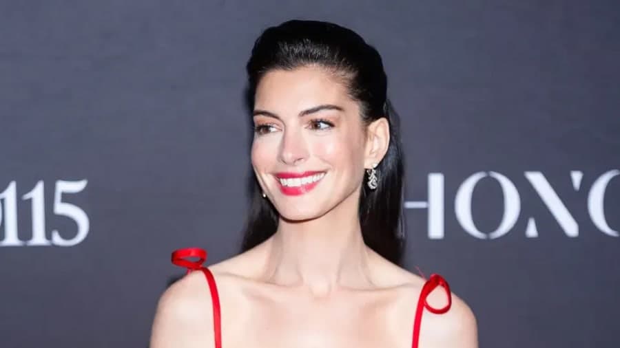 Anne Hathaway wearing a white flowing maxi skirt and cropped wrap top with billowing sleeves, revealing her baby bump while accessorising with gold bangles