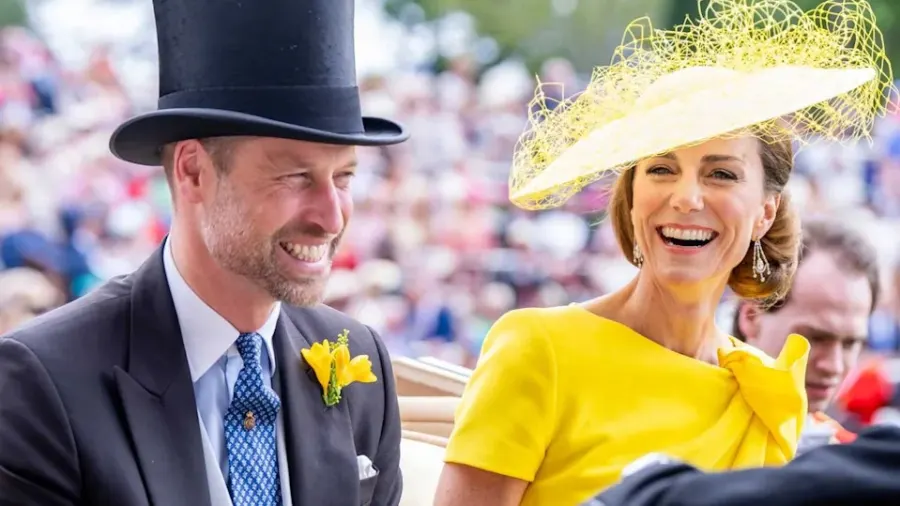 A man and woman dressed in smart casual clothing stand together at an outdoor public event, smiling and engaged with the crowd around them