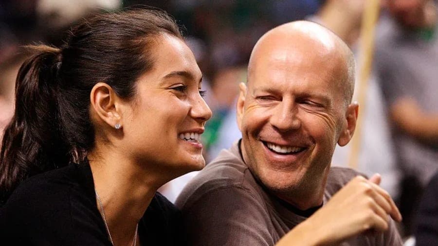 Emma Heming Willis wearing a birthday party hat alongside Bruce Willis, both smiling during a birthday celebration at home