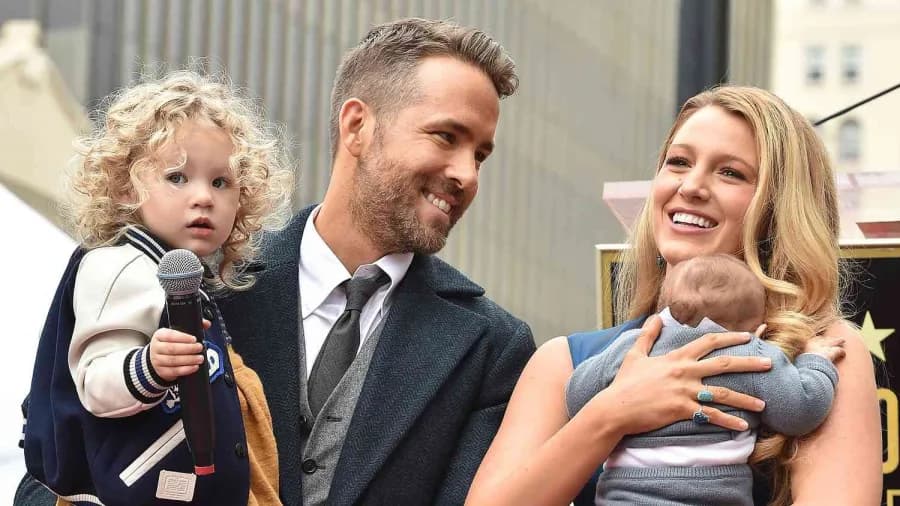 A man in casual clothing poses with a woman in a summery outfit, both smiling warmly, surrounded by young children whose faces are not visible in the image