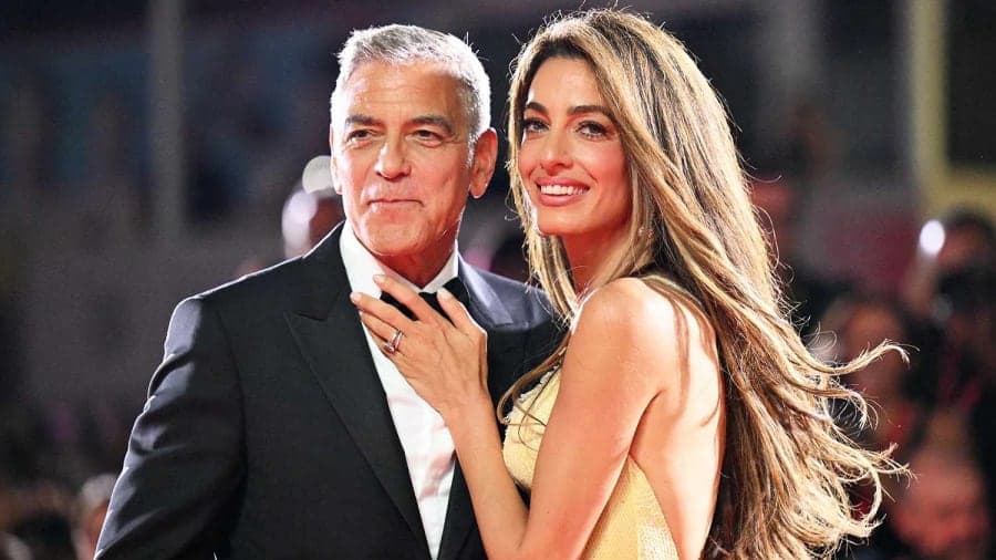 A man in a grey suit and a woman in a black embroidered dress stepping off a boat onto a lakeside dock, against a scenic Italian lake backdrop.
