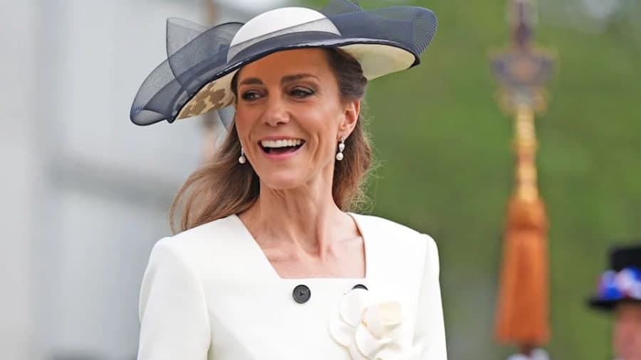 A woman in an elegant coat dress waves to a crowd at a formal public engagement, her dark hair neatly styled