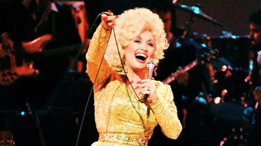 A large crowd gathered at an outdoor venue, with a stage lit in warm golden light and a rhinestone-studded costume on display