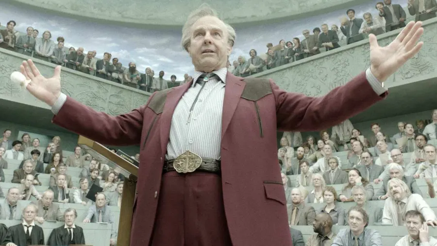 A promotional still from a major Hollywood film showing a heavyset older man in a Stetson hat standing in a large, dramatically lit interior space